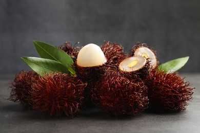 Photo of Delicious ripe rambutans and green leaves on grey table, closeup