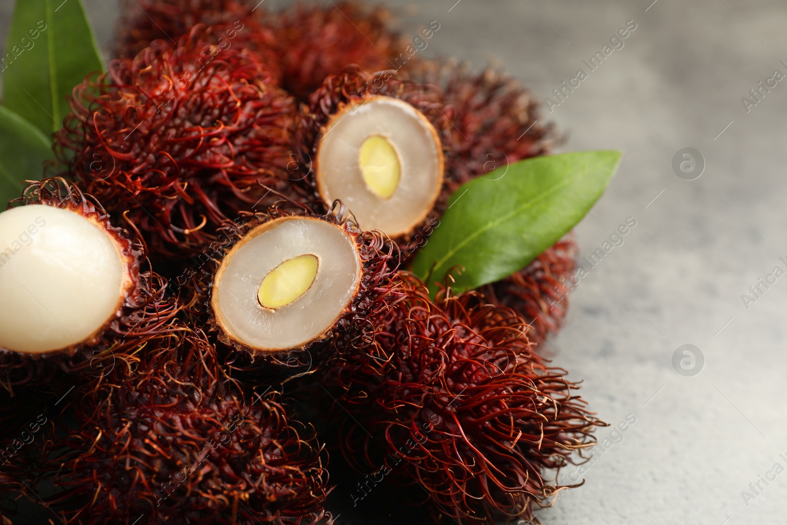 Photo of Delicious ripe rambutans and green leaves on grey table, closeup. Space for text