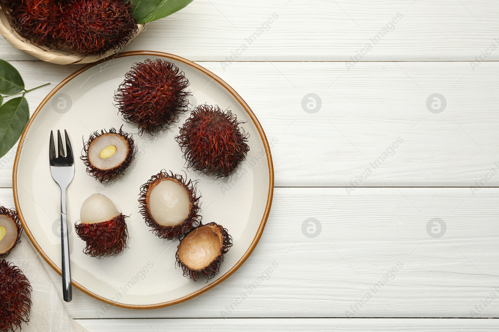 Photo of Delicious ripe rambutans served on white wooden table, flat lay. Space for text