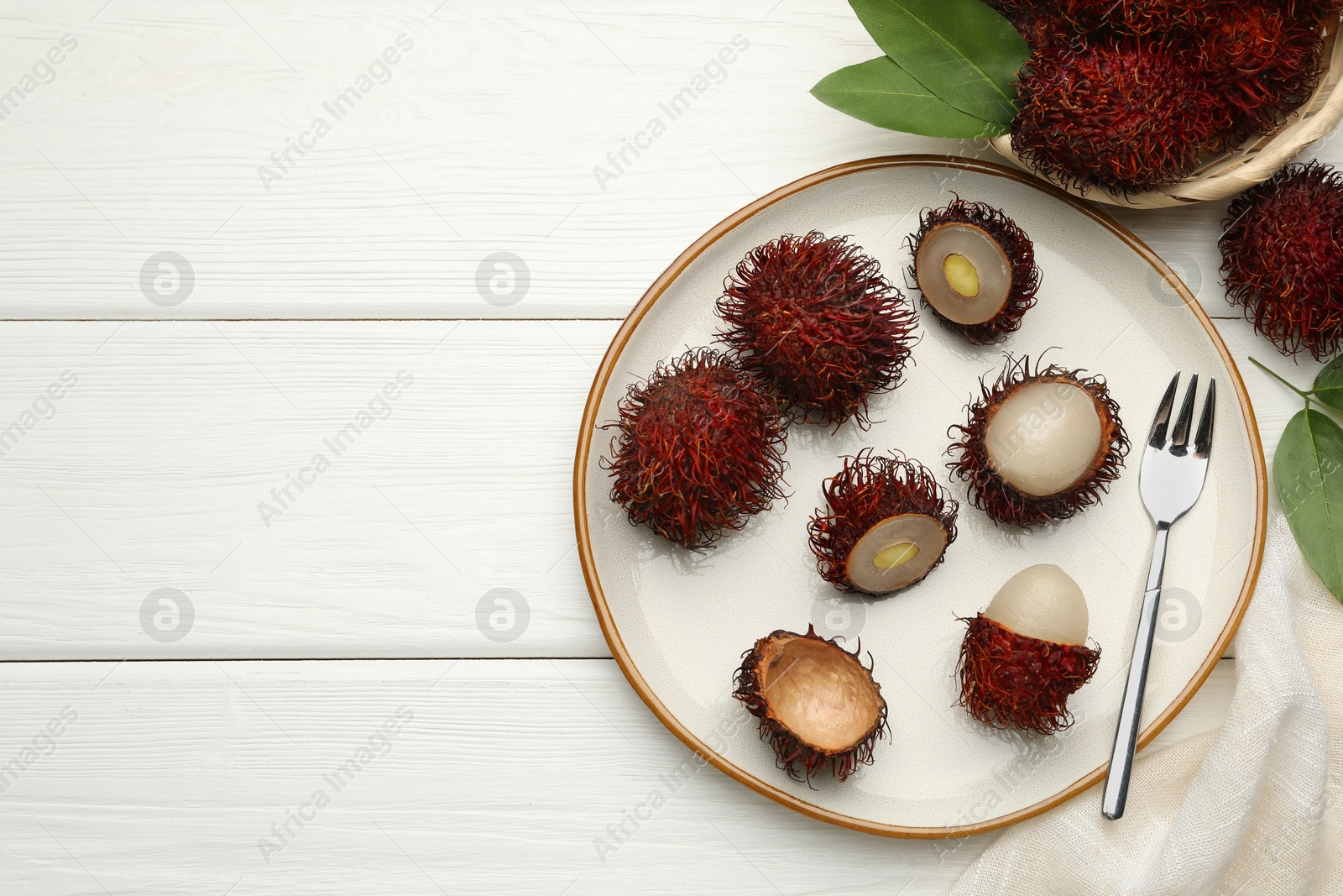 Photo of Delicious ripe rambutans served on white wooden table, flat lay. Space for text