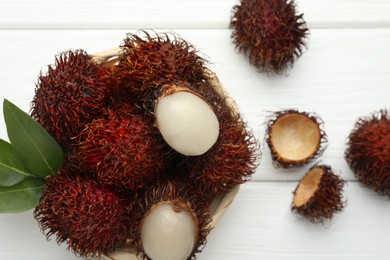 Photo of Delicious ripe rambutans and green leaves on white wooden table, flat lay