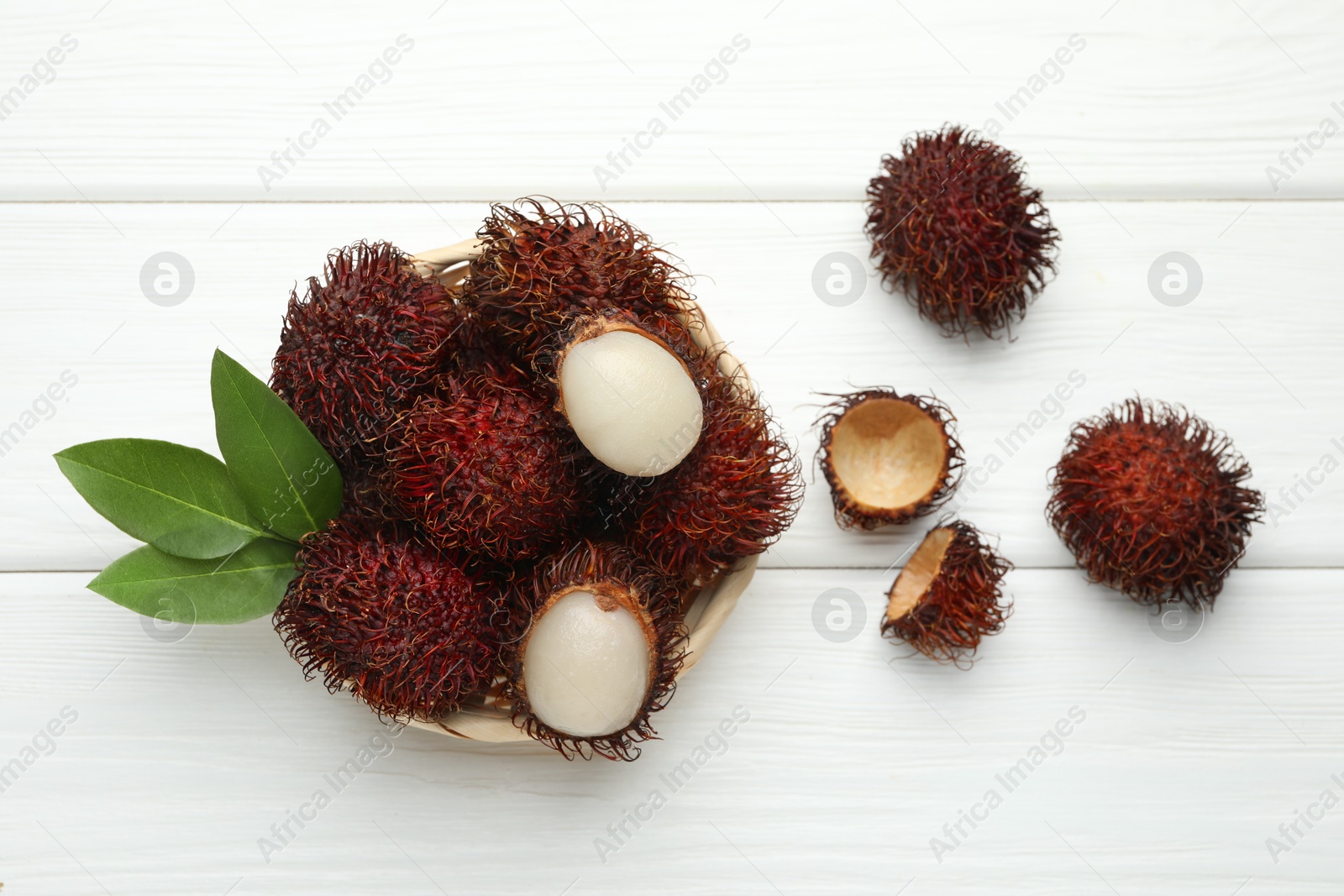 Photo of Delicious ripe rambutans and green leaves on white wooden table, flat lay