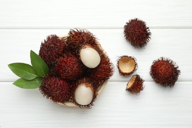 Delicious ripe rambutans and green leaves on white wooden table, flat lay