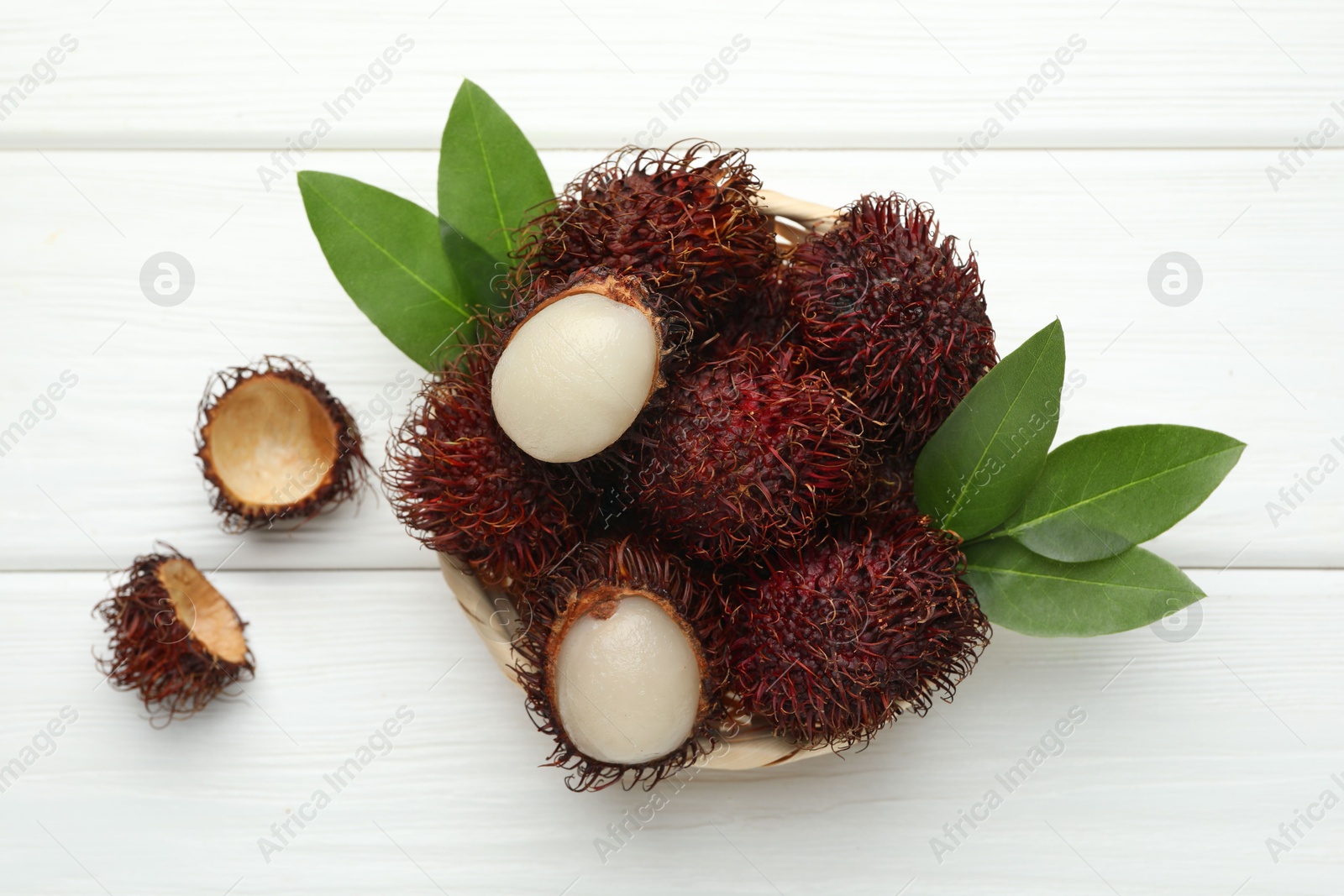 Photo of Delicious ripe rambutans and green leaves on white wooden table, top view