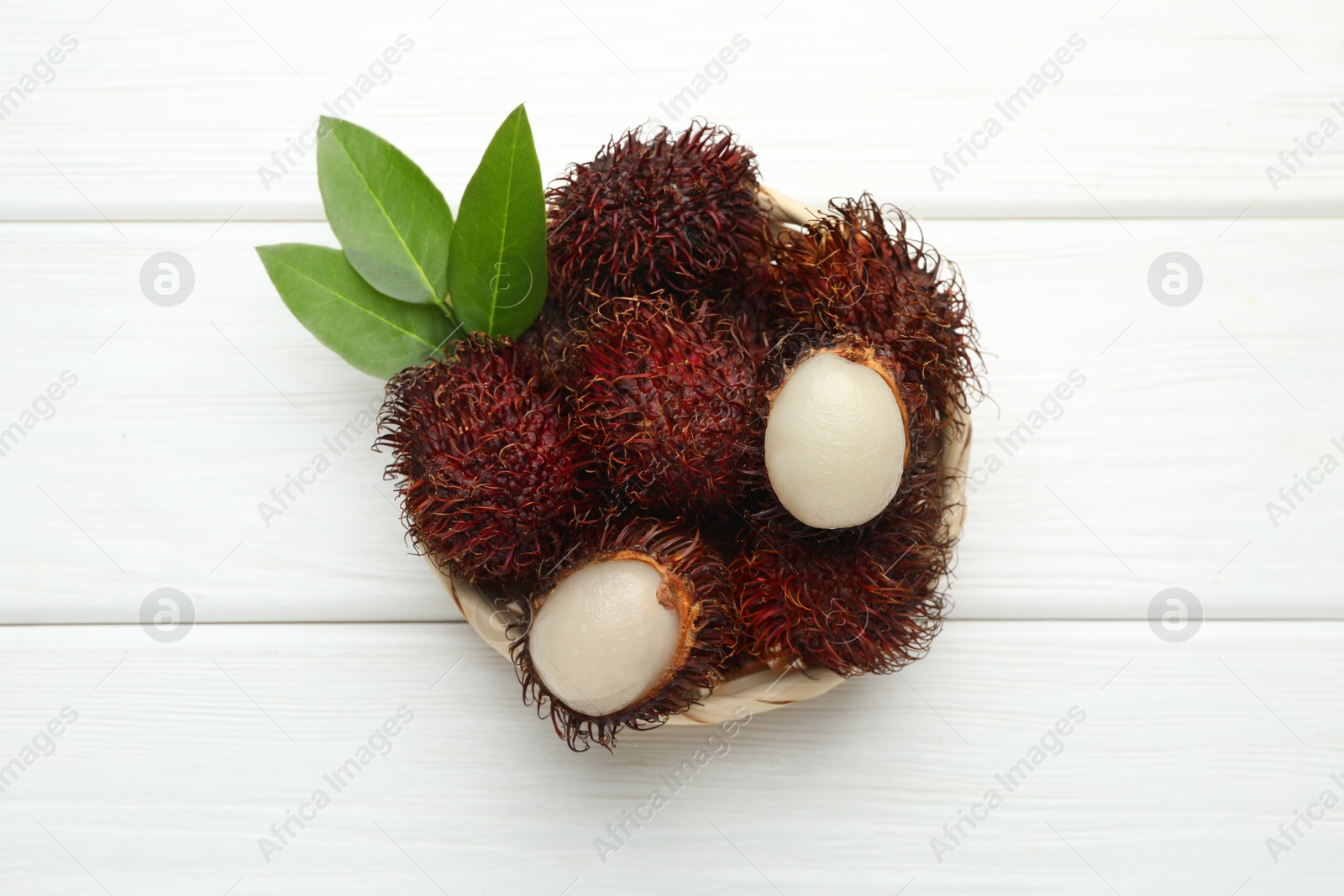 Photo of Delicious ripe rambutans and green leaves on white wooden table, top view