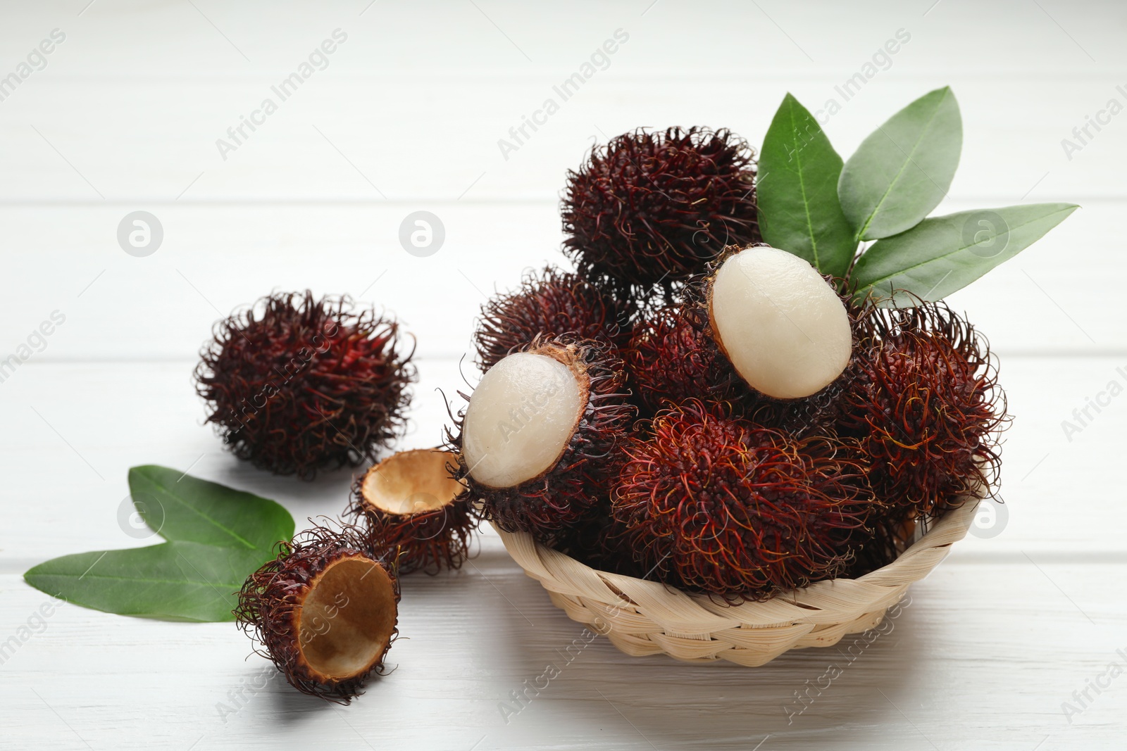 Photo of Delicious ripe rambutans and green leaves on white wooden table, closeup