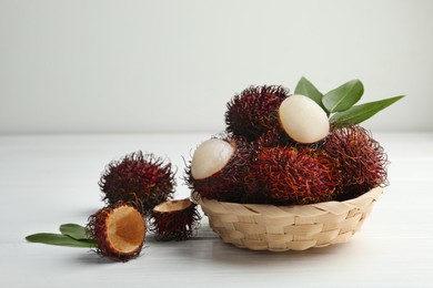 Photo of Delicious ripe rambutans and green leaves on white wooden table