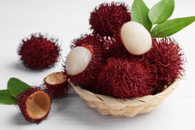 Photo of Delicious ripe rambutans and green leaves on white wooden table, closeup