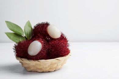 Photo of Delicious ripe rambutans and green leaves on white wooden table, closeup. Space for text