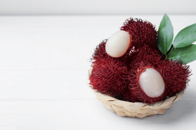 Photo of Delicious ripe rambutans and green leaves on white wooden table, closeup. Space for text