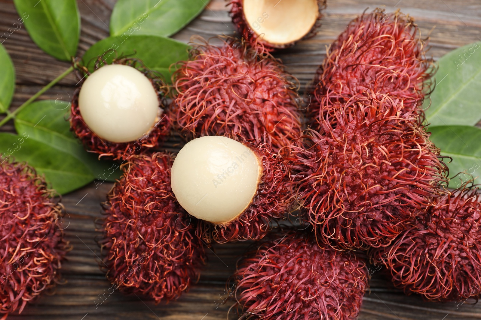 Photo of Delicious ripe rambutans and green leaves on wooden table, flat lay