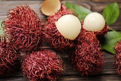 Photo of Delicious ripe rambutans and green leaves on wooden table, closeup