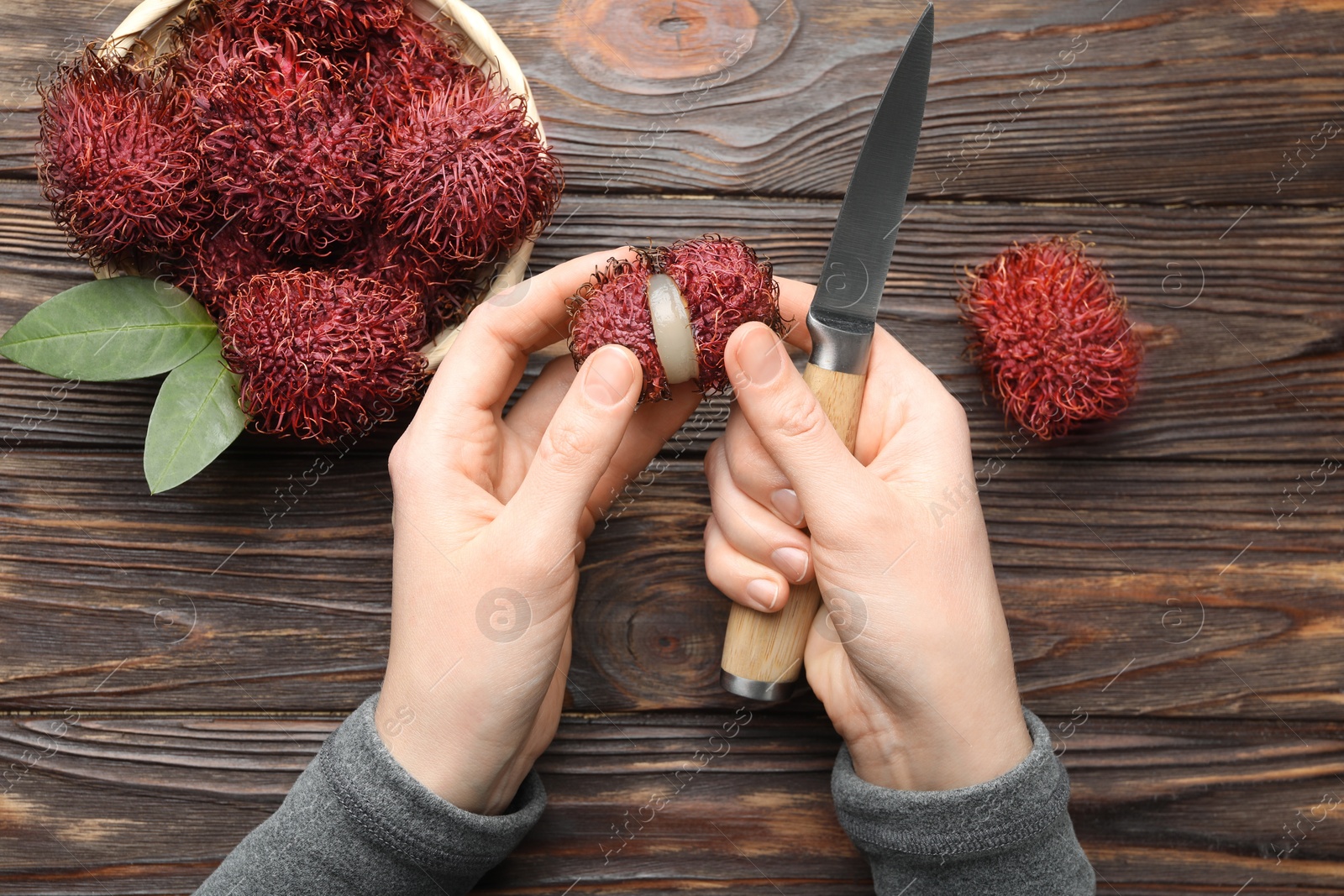 Photo of Woman peeling ripe rambutan at wooden table, top view