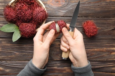 Photo of Woman peeling ripe rambutan at wooden table, top view