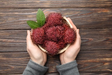 Photo of Woman with ripe rambutans at wooden table, top view