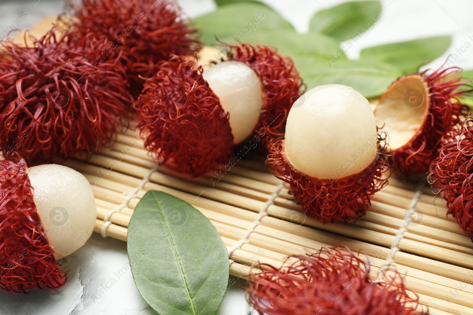 Photo of Delicious ripe rambutans and green leaves on white marble table, closeup