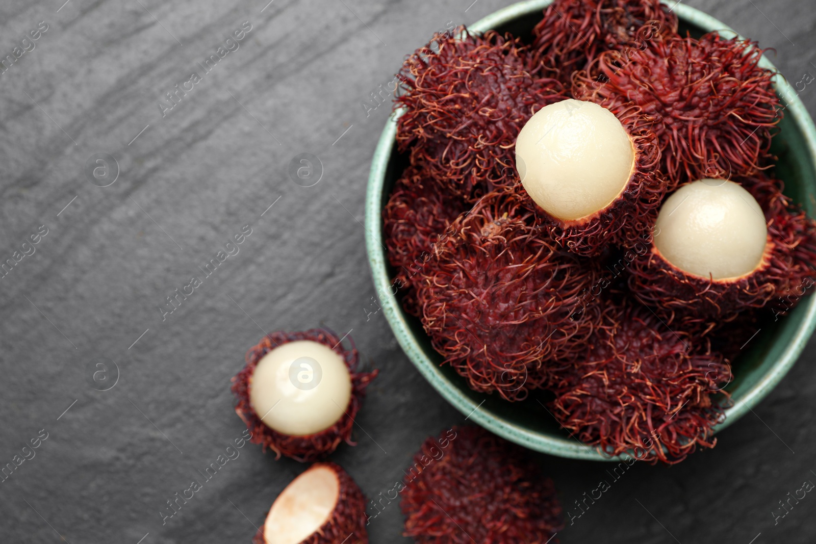 Photo of Delicious ripe rambutans in bowl on black table, top view. Space for text