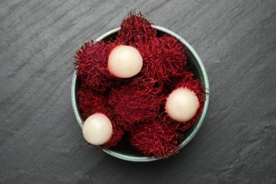 Photo of Delicious ripe rambutans in bowl on black table, top view