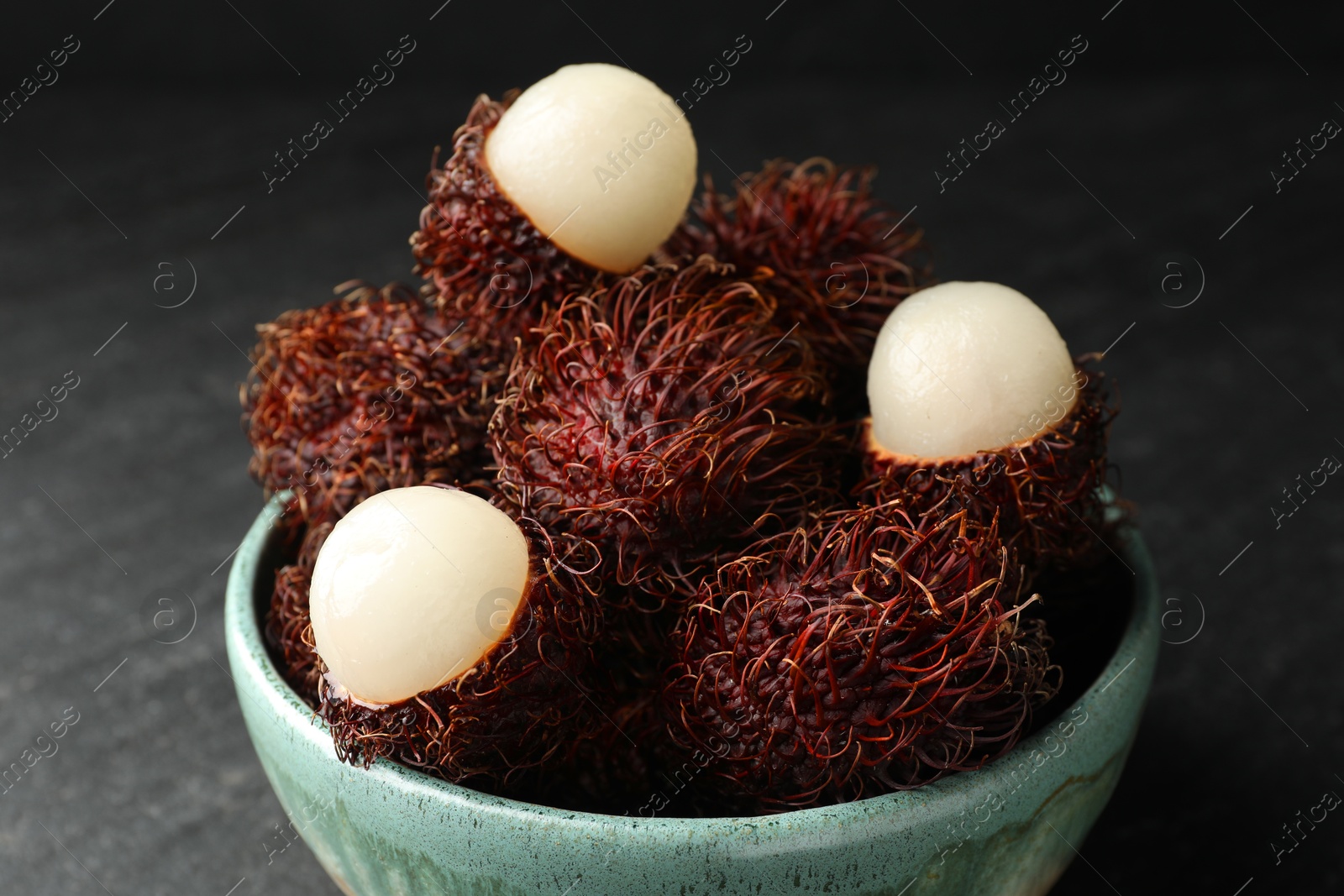 Photo of Delicious ripe rambutans in bowl on black table, closeup