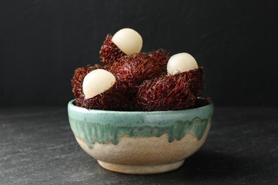 Photo of Delicious ripe rambutans in bowl on black table, closeup