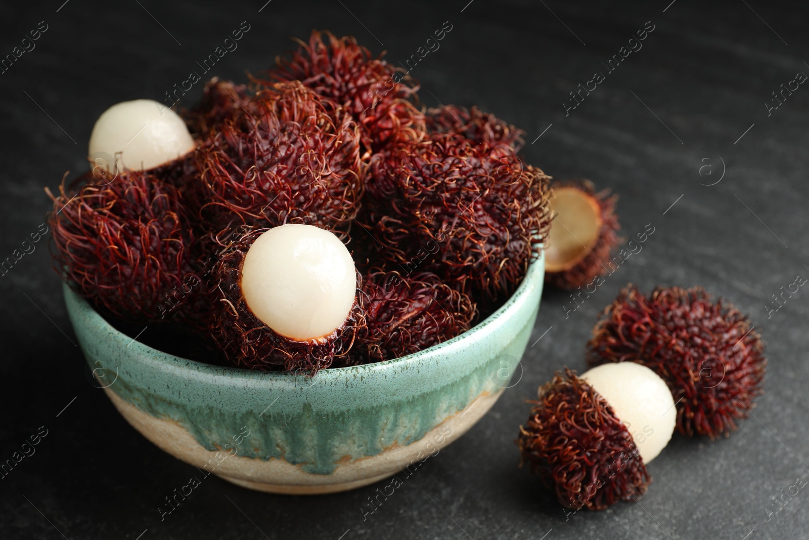 Photo of Delicious ripe rambutans in bowl on black table, closeup