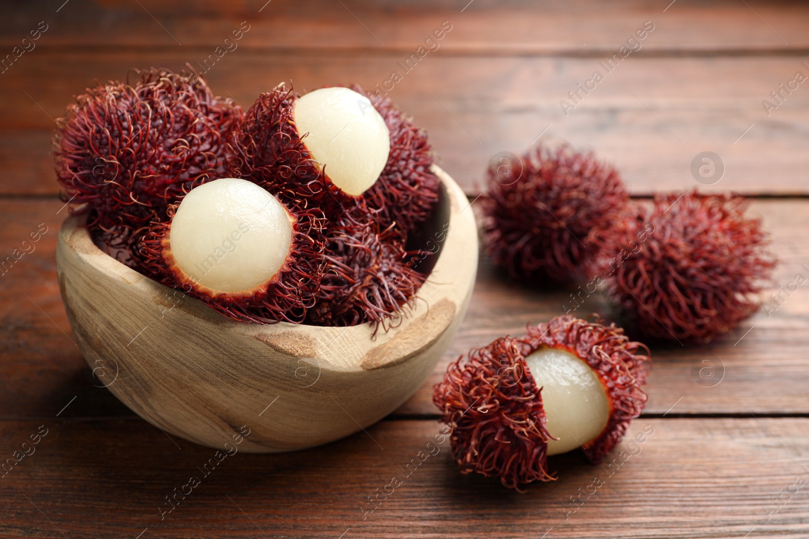 Photo of Delicious ripe rambutans in bowl on wooden table, closeup