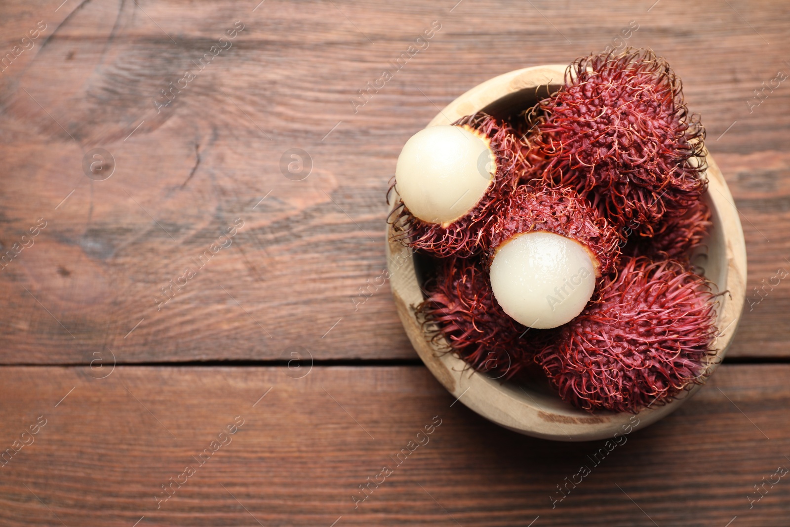 Photo of Delicious ripe rambutans in bowl on wooden table, top view. Space for text