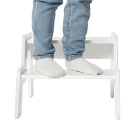 Photo of Little boy standing on step stool against white background, closeup