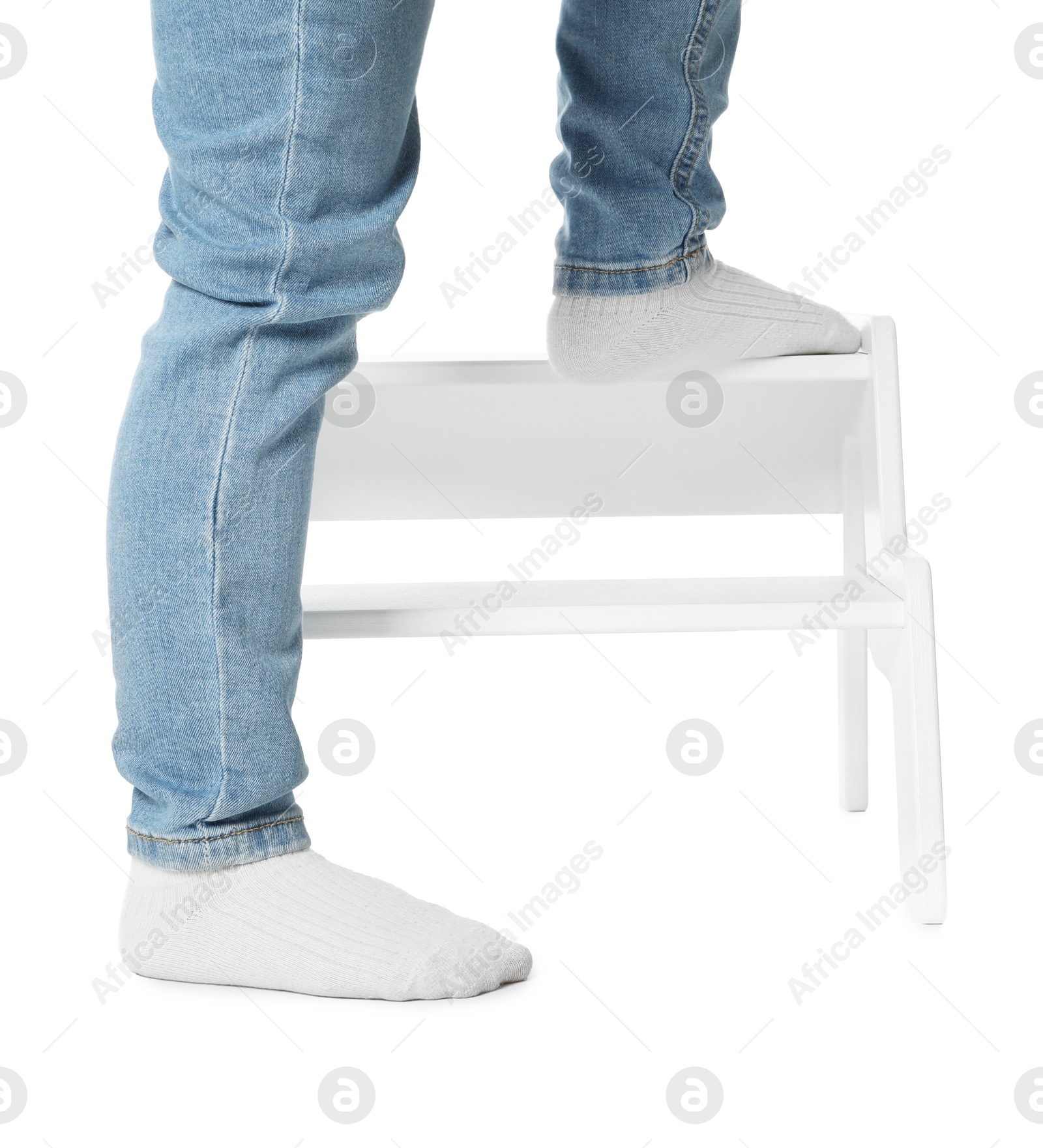 Photo of Little boy standing on step stool against white background, closeup