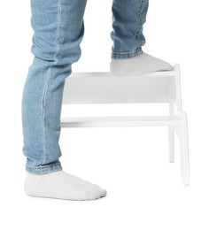 Photo of Little boy standing on step stool against white background, closeup