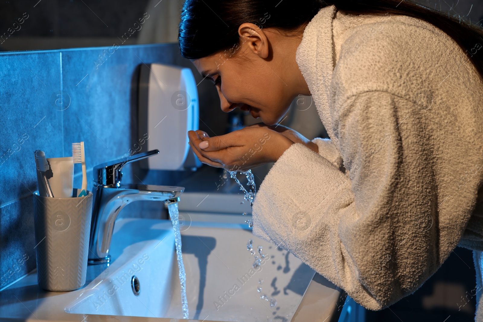 Photo of Woman washing her face over sink in bathroom