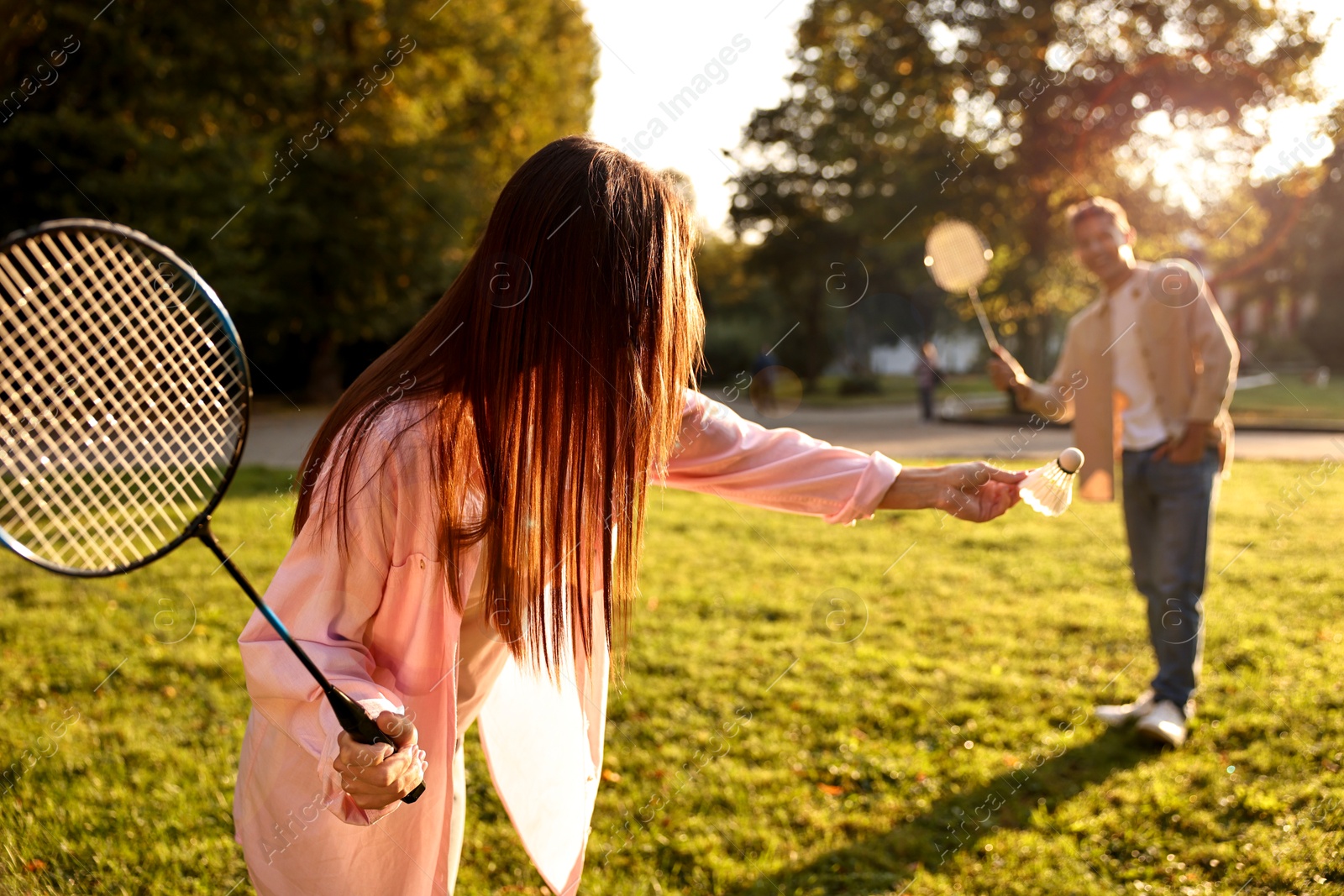 Photo of Young woman and man playing badminton in park on sunny day, selective focus