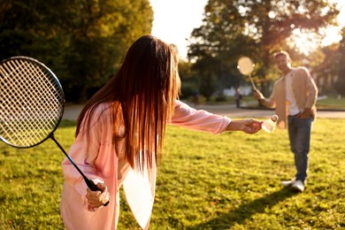 Photo of Young woman and man playing badminton in park on sunny day, selective focus