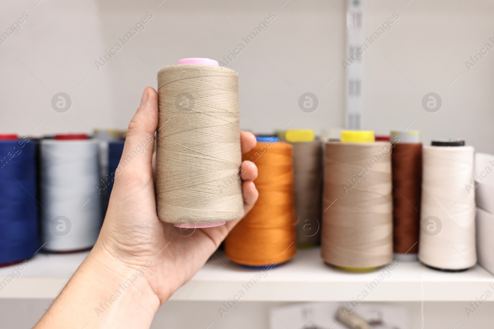 Photo of Woman holding spool of thread near shelf in professional workshop, closeup