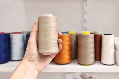 Photo of Woman holding spool of thread near shelf in professional workshop, closeup