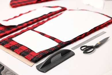 Photo of Pieces of fabric, measurements, scissors and other tools on white table in professional workshop, closeup