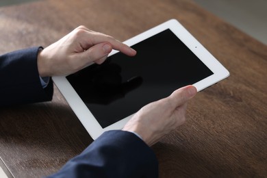 Photo of Businessman using tablet at wooden table, closeup. Modern technology