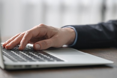 Photo of Businessman using laptop at table indoors, closeup. Modern technology