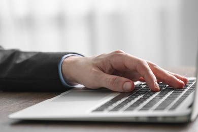 Photo of Businessman using laptop at table indoors, closeup. Modern technology