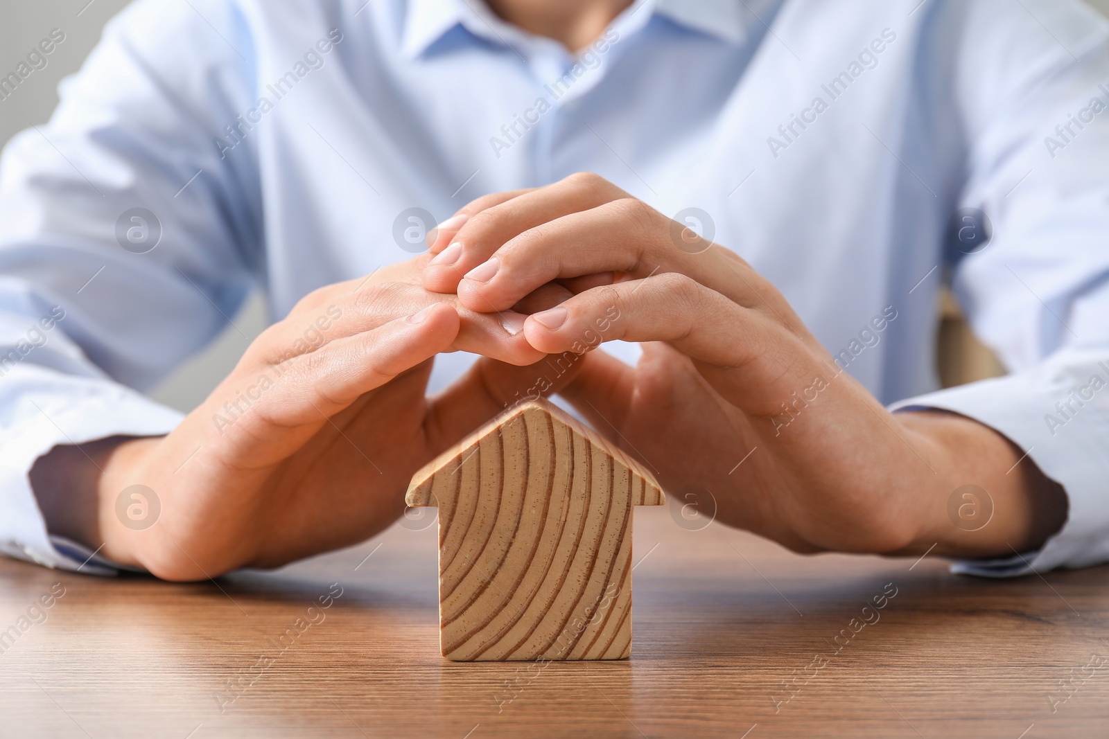 Photo of Real estate insurance. Man with wooden house figure at table, closeup