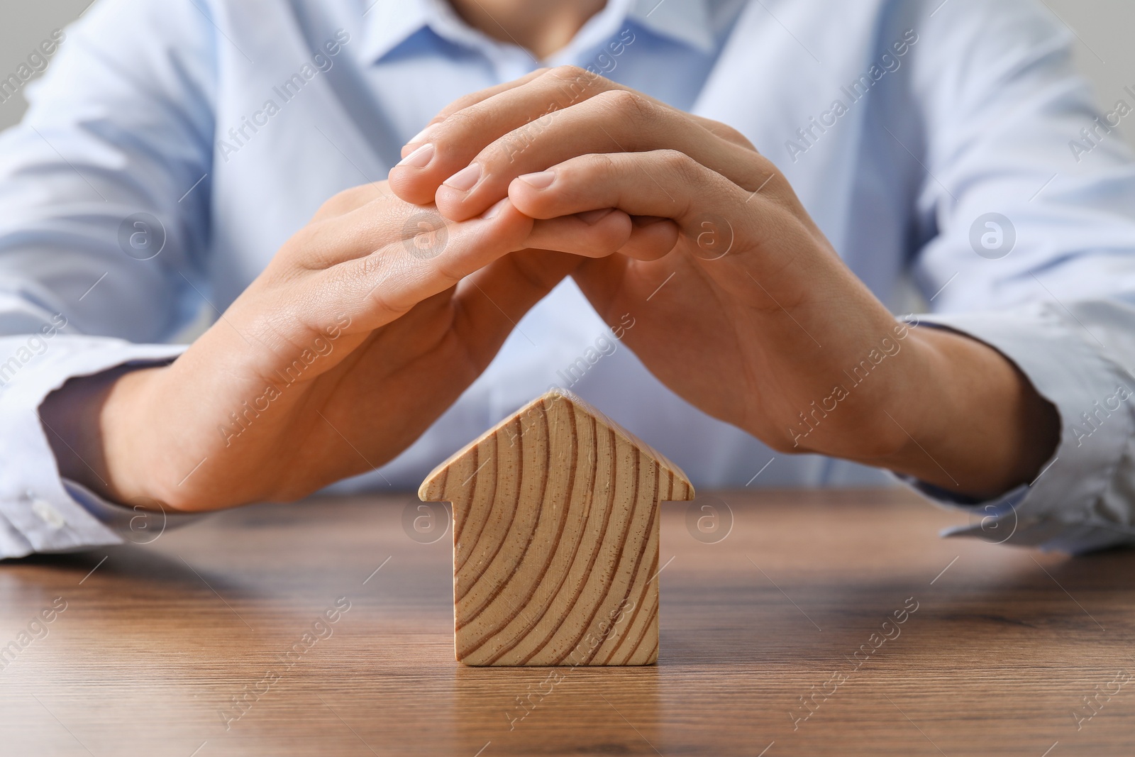 Photo of Real estate insurance. Man with wooden house figure at table, closeup