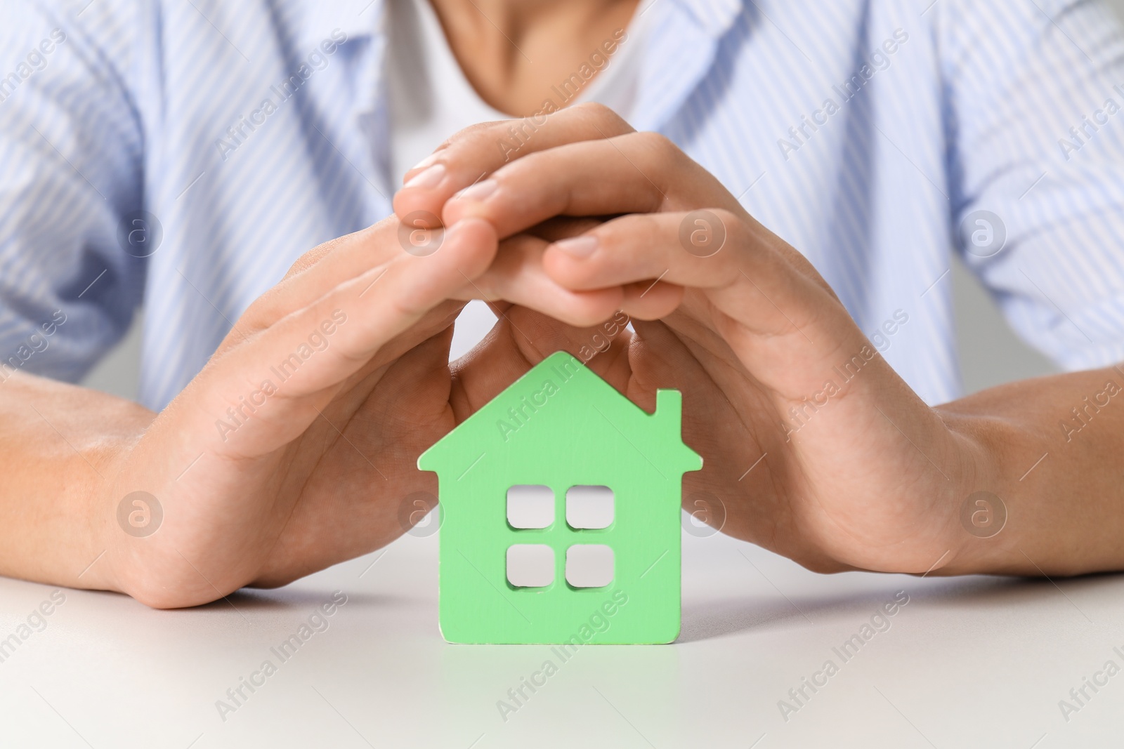 Photo of Real estate insurance. Man with green house figure at light table, closeup