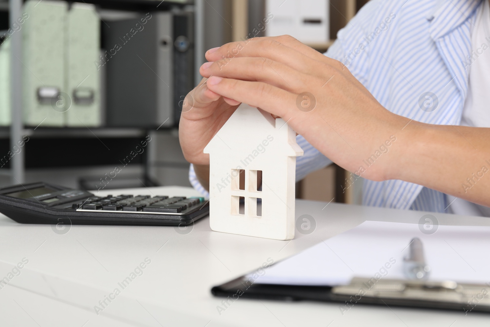 Photo of Real estate insurance. Man with wooden house figure at light table, closeup