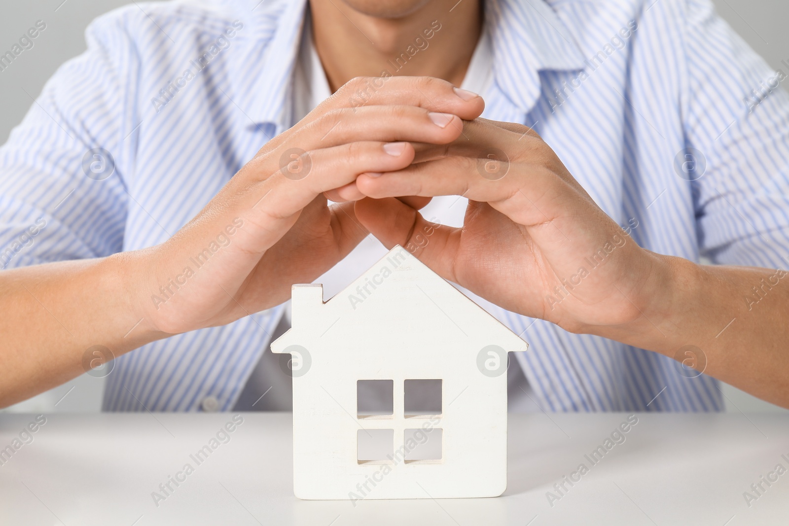 Photo of Real estate insurance. Man with wooden house figure at light table, closeup