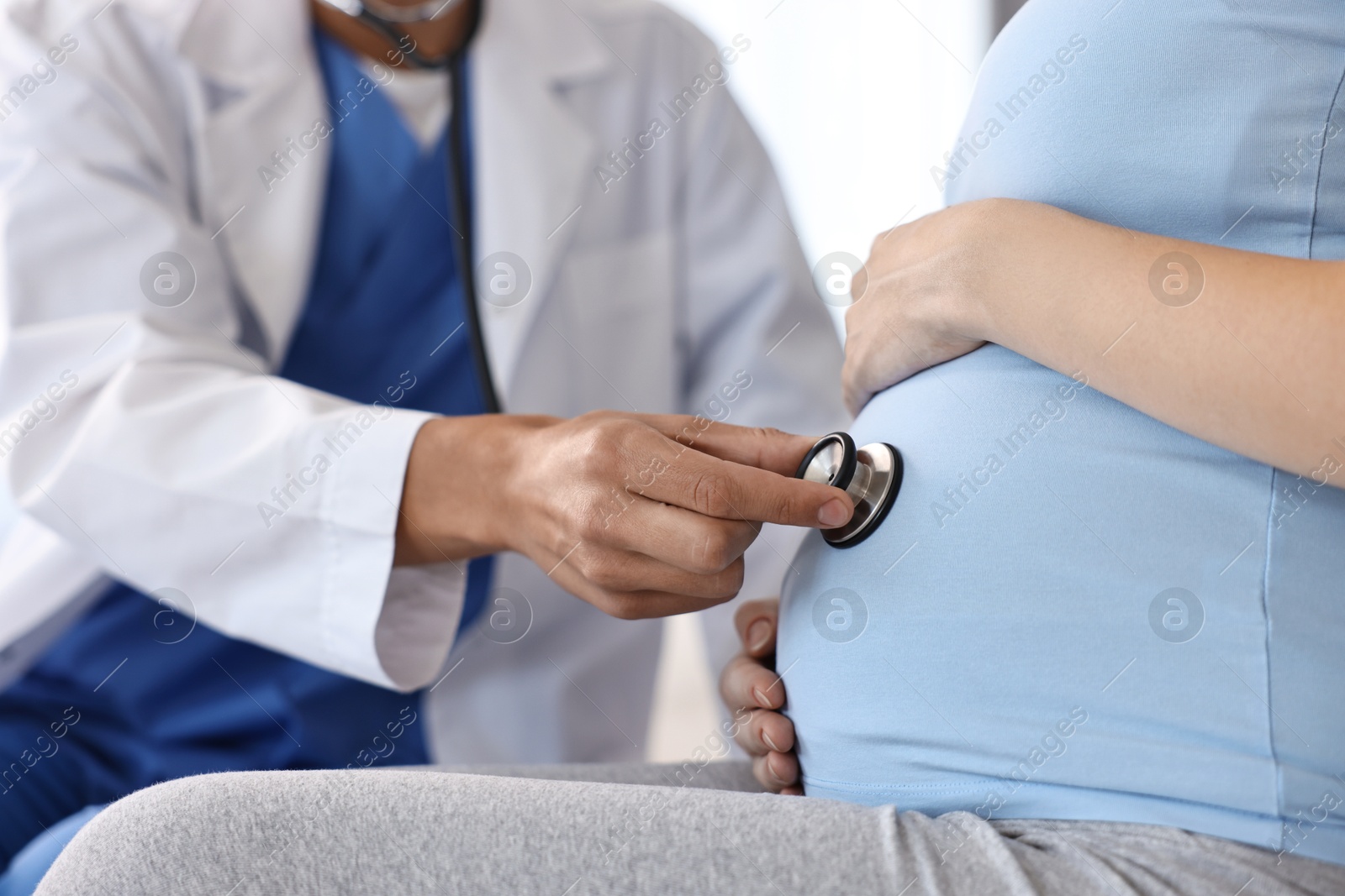 Photo of Pregnancy checkup. Doctor with stethoscope listening baby's heartbeat in patient's tummy indoors, closeup