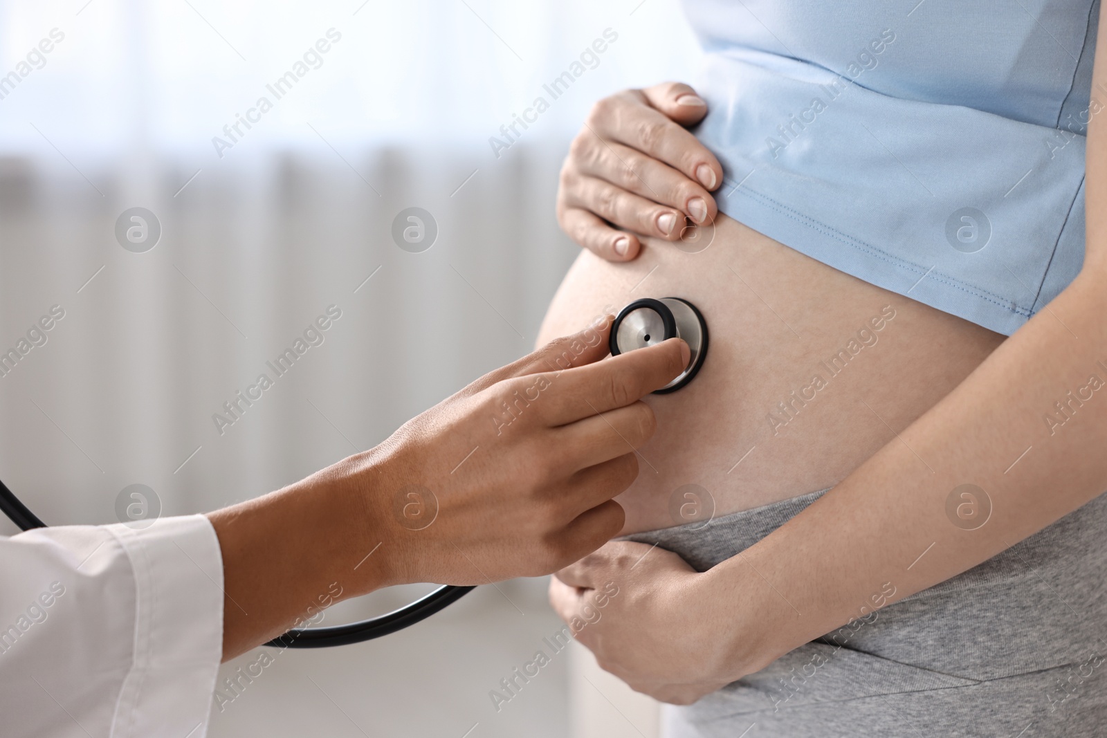 Photo of Pregnancy checkup. Doctor with stethoscope listening baby's heartbeat in patient's tummy indoors, closeup