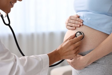 Photo of Pregnancy checkup. Smiling doctor with stethoscope listening baby's heartbeat in patient's tummy indoors, closeup