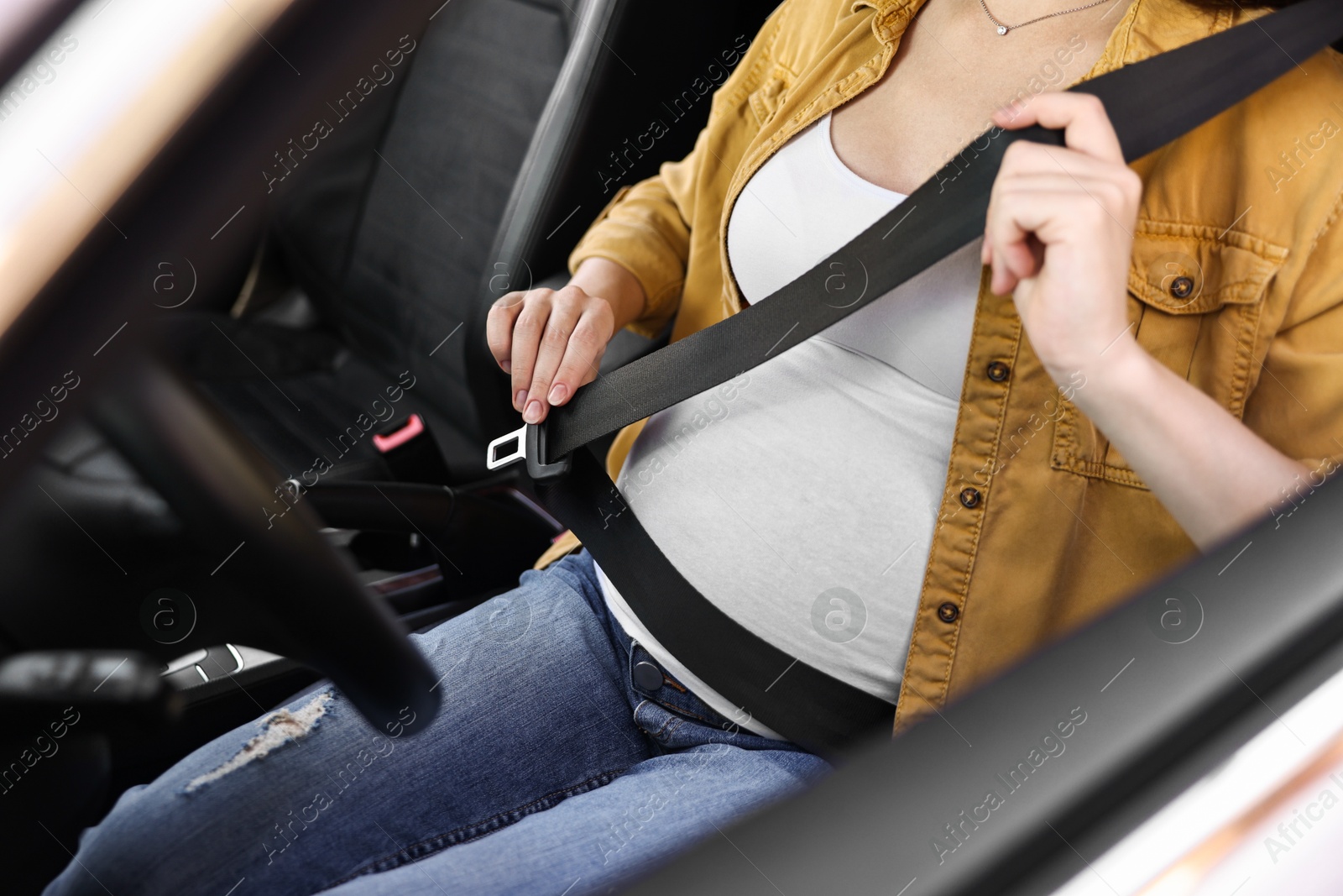 Photo of Pregnant woman fastening safety belt in car, closeup