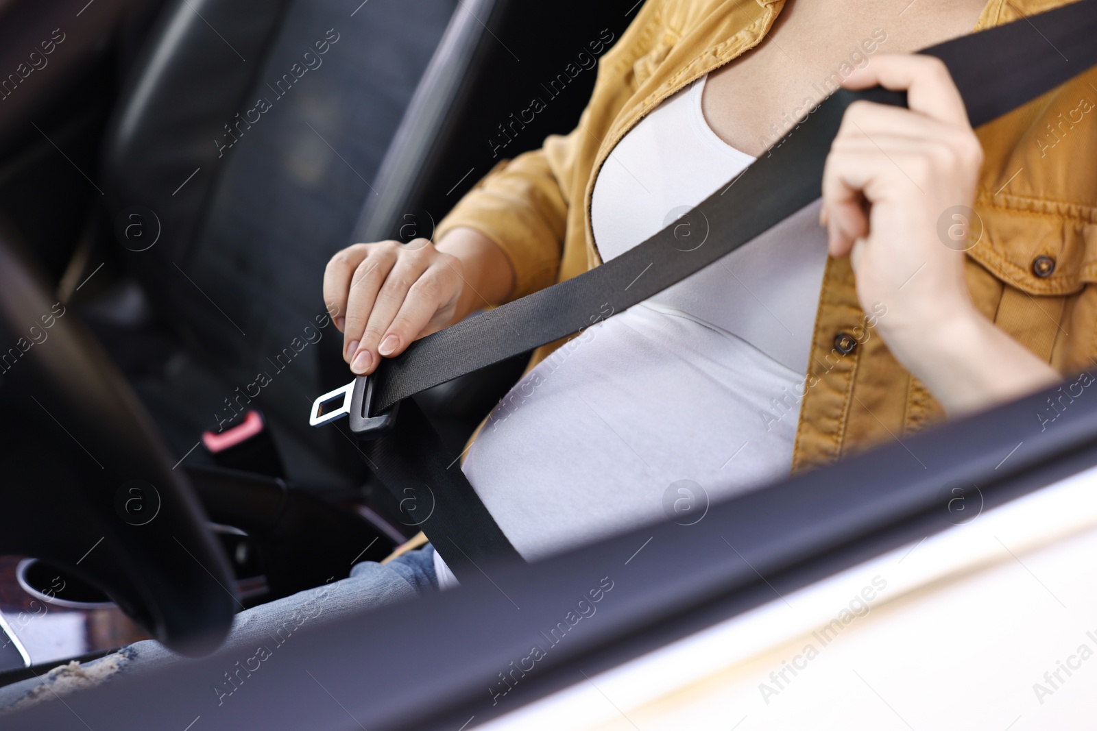 Photo of Pregnant woman fastening safety belt in car, closeup