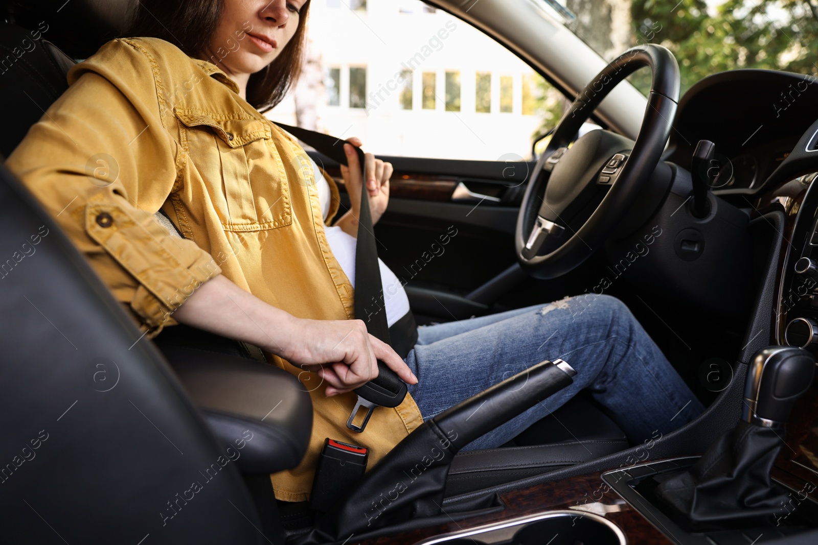 Photo of Pregnant woman fastening safety belt in car, closeup